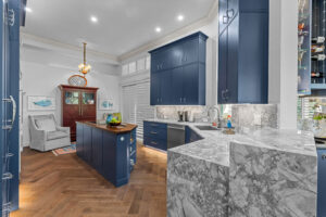 Luxury kitchen interior featuring custom navy blue cabinetry, elegant marble countertops, and a large kitchen island with wood flooring.